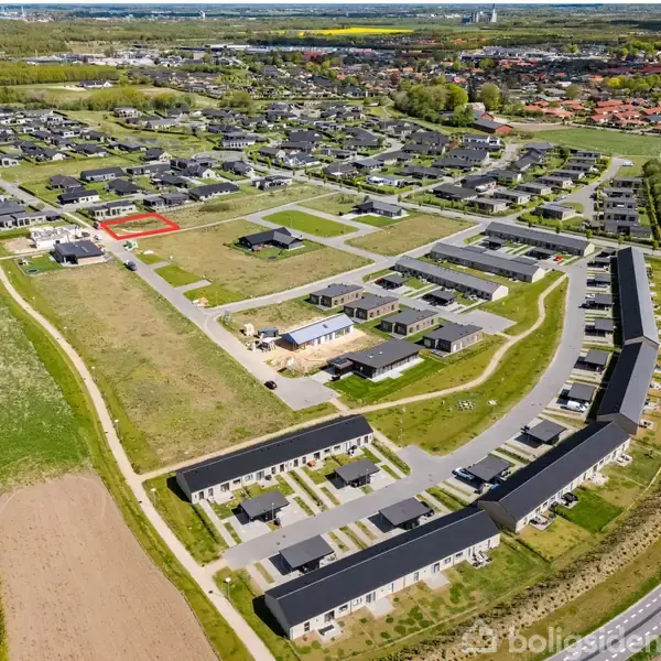 Boligområde med moderne huse omgivet af grønne arealer. Nogle veje og stier forbinder bygningerne, mens åbne marker og skove ligger i nærheden. En vej ses tydeligt i nederste højre hjørne.