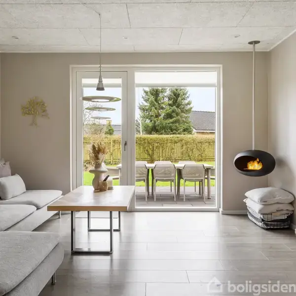 Gråt sofaarrangement står nær et sofabord med planter, vendt mod en vægmonteret fladskærm i en lys stue. Store glasdøre fører ud til en have med et træbord og stole.