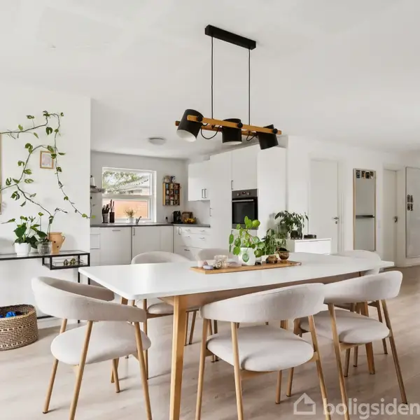 Et lyst, moderne spisekøkken med et hvidt bord omgivet af seks stole. En sort pendellampe hænger over bordet. Planter pynter rummet, og et hjørne af køkkenet ses i baggrunden.