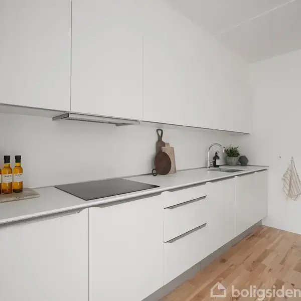 Et moderne køkken med hvide skabe og integreret komfur; flasker og skærebrætter står på bordet. Trægulv og indbygget ovn skaber en minimalistisk og elegant atmosfære.