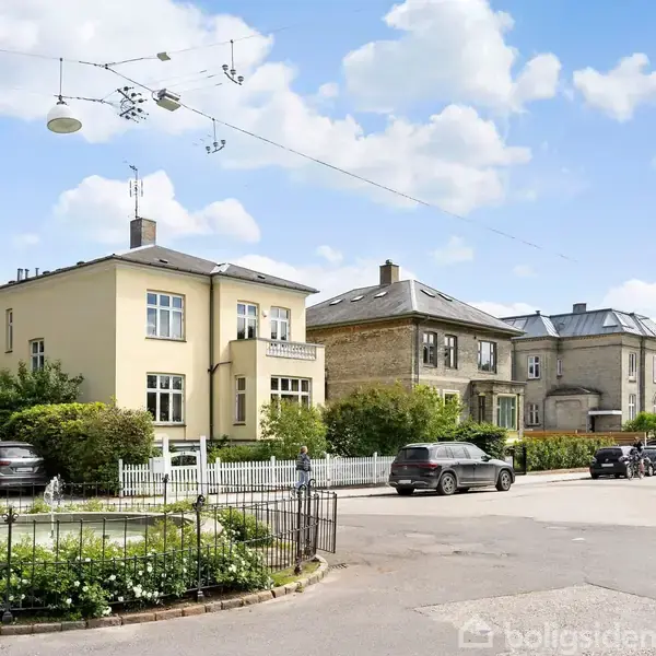 En stue med en sort sofa og to lysebrune stole omkring et ovalt træbord. Der er kunst på de lillarøde vægge, en kommode, og en fransk dør åbner mod et lysere værelse.
