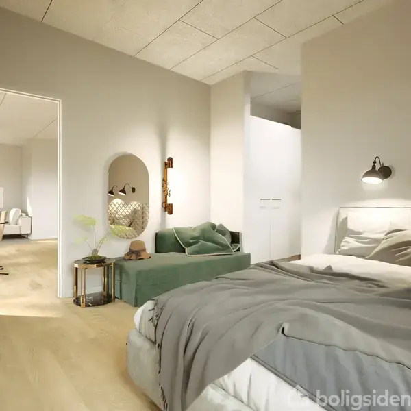 Soveværelse med dobbeltseng i forgrunden, dækket af gråt sengetøj og puder. I midten ses en grøn sofa og rundt spejl. I baggrunden fører en åbning til et andet rum.