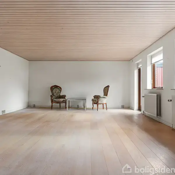 To antikke stole står ved et lille bord på et trægulv i en stor, lys stue med hvidmalede vægge og et træloft. Flere vinduer trækker dagslys ind.