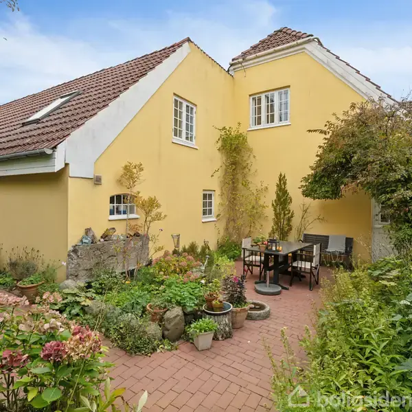 Et badeværelse med et toilet står ved siden af en kurv og en plante. Vasken har et spejl over sig. Hylde med planter hænger på væggen i et skråt loftsrum.