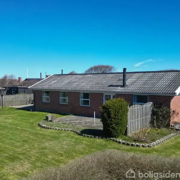En en-families bolig af mursten med skråt, teglbelagt tag står omgivet af en velplejet græsplæne og indhegnede haver i et roligt beboelseskvarter.