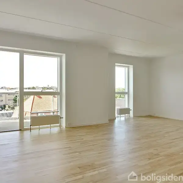 Et lyst rum med trægulv har åbne vinduer, der vender ud mod en balkon. Sollys strømmer ind og oplyser det minimalistiske miljø.