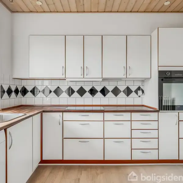 Hvidt køkken med trækanter, har et indbygget ovn, hvide fliser med sorte diamantmønstre som backsplash, stålvask ved vindue, og lyst trægulv.