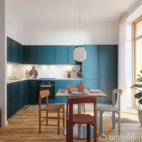 Køkken med blå skabe omgiver et spisebord med forskellige stole. En lampe hænger over bordet. Planter og dekorationer skaber en hyggelig atmosfære. Sollys skinner ind fra store vinduer.