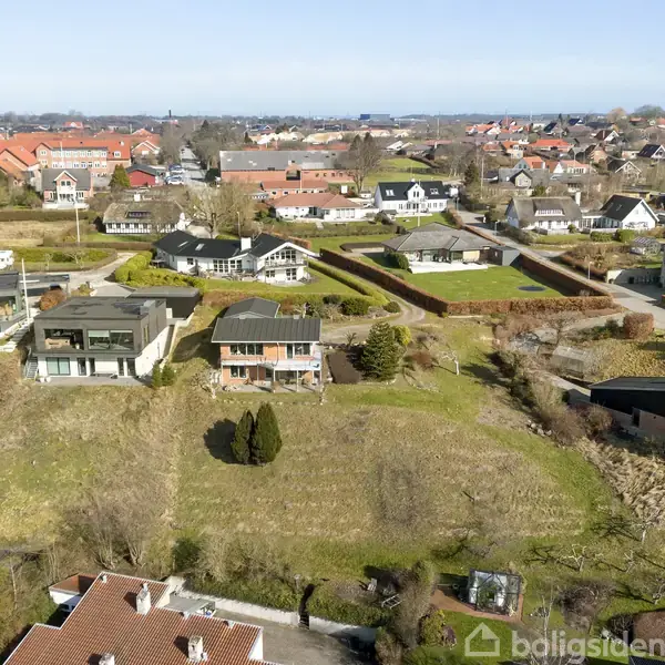 Huse står stille i en forstadsbebyggelse med velplejede haver og grønne områder. Områdtet er præget af moderne og traditionelle bygninger. Landskabet er åbent med udsigt over flere hustage.