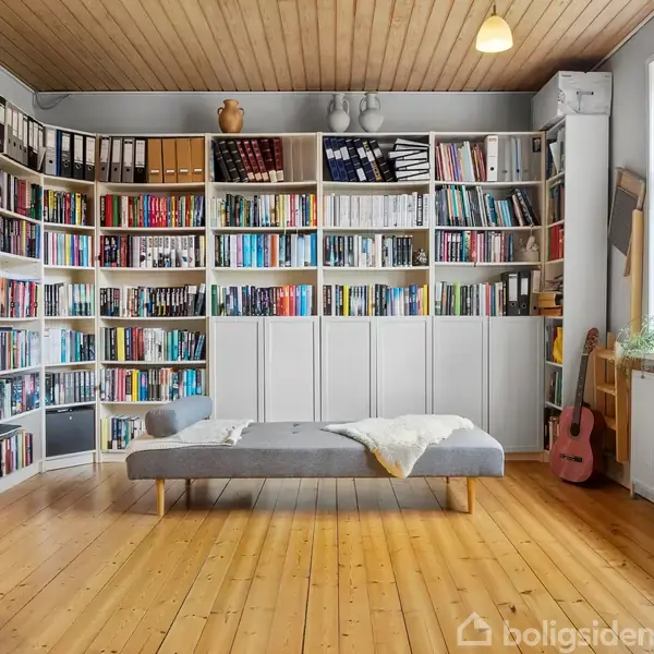 Hylde fyldt med bøger og mapper står mod væggen. En grå daybed er placeret foran hylden. Rummet har trægulv og et vindue med naturligt lys, samt en rosa guitar.