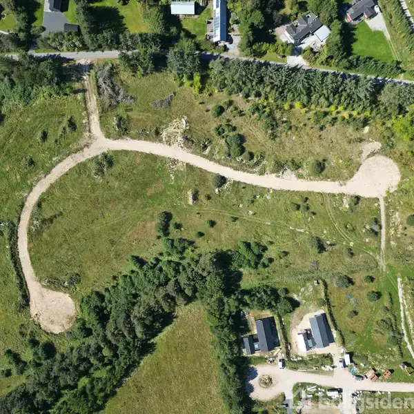 Luftfoto viser et landdistrikt (objekt) med spredte huse og veje (handling) nær en kystlinje med havet i horisonten (kontekst).