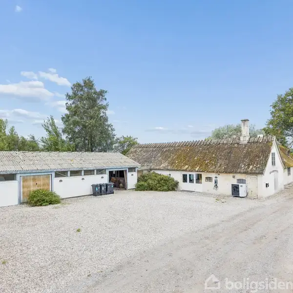 Et lyst, moderne rum med store gulv-til-loft-vinduer, der viser en frodig have udenfor. To sorte stole står i rummet nær åbne døre, og planter dekorerer hjørnerne.