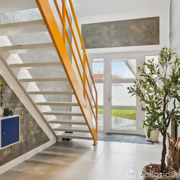 En trappe med gule gelændere fører opad i en lys entre. Til venstre er der blå skabe. En grøn plante står ved siden af en glasdør, hvorpå "EOVIND" er skrevet.