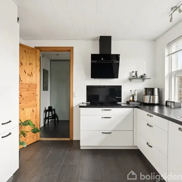 Et hus med skråt tag i en have. Huset er omgivet af græsplæne, buske og et flagstang. Omkringliggende huse ses i baggrunden under en blå himmel.
