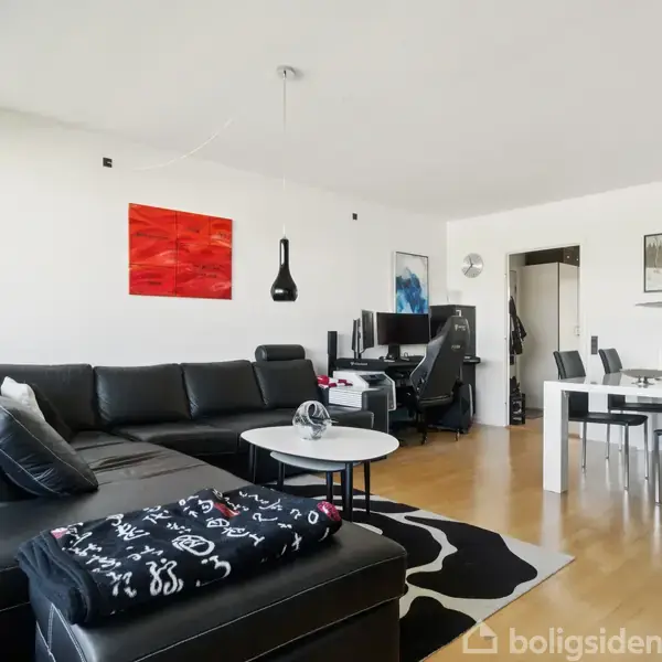 Sort læderhjørnesofa med tæppe ligger i stuen. Rundt sofabord og tæppe ved siden af. Spisebord med stole til højre, moderne kunst på væggen.